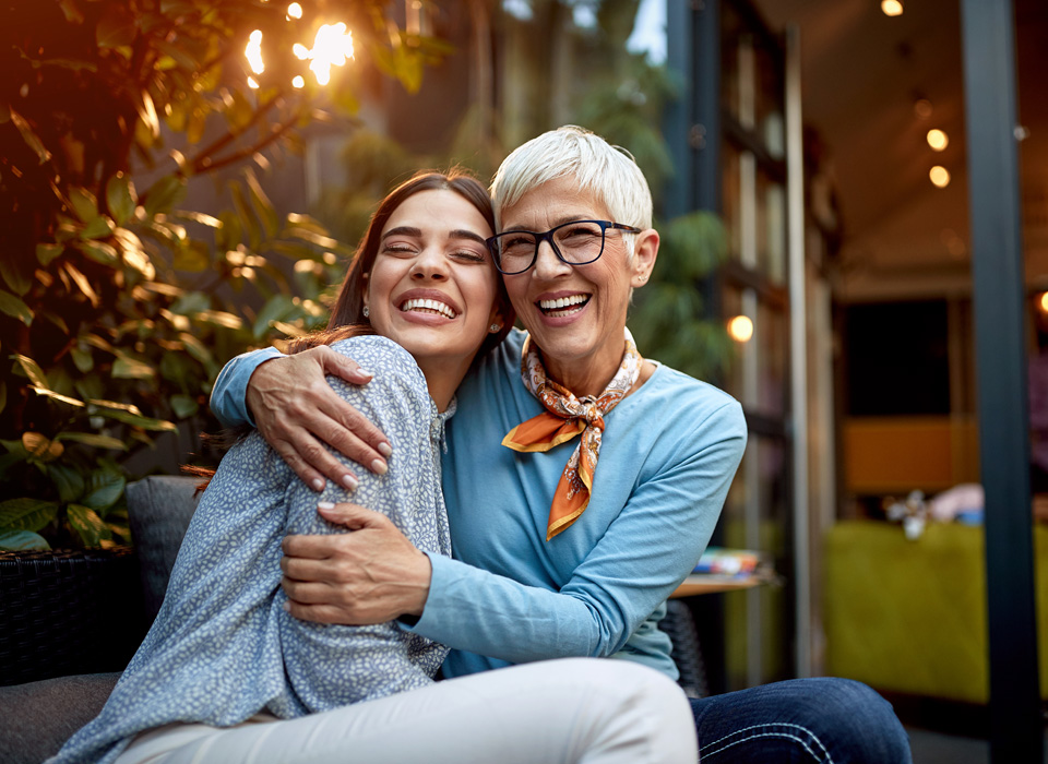 Senior mother and adult daughter, hugging and smiling.