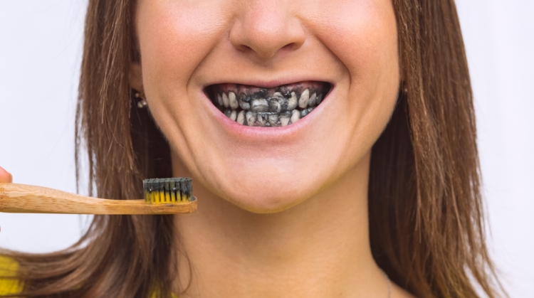 Woman brushing teeth with charcoal toothpaste, showing black-stained smile – Vistoso Dental Partners, Oro Valley, AZ.